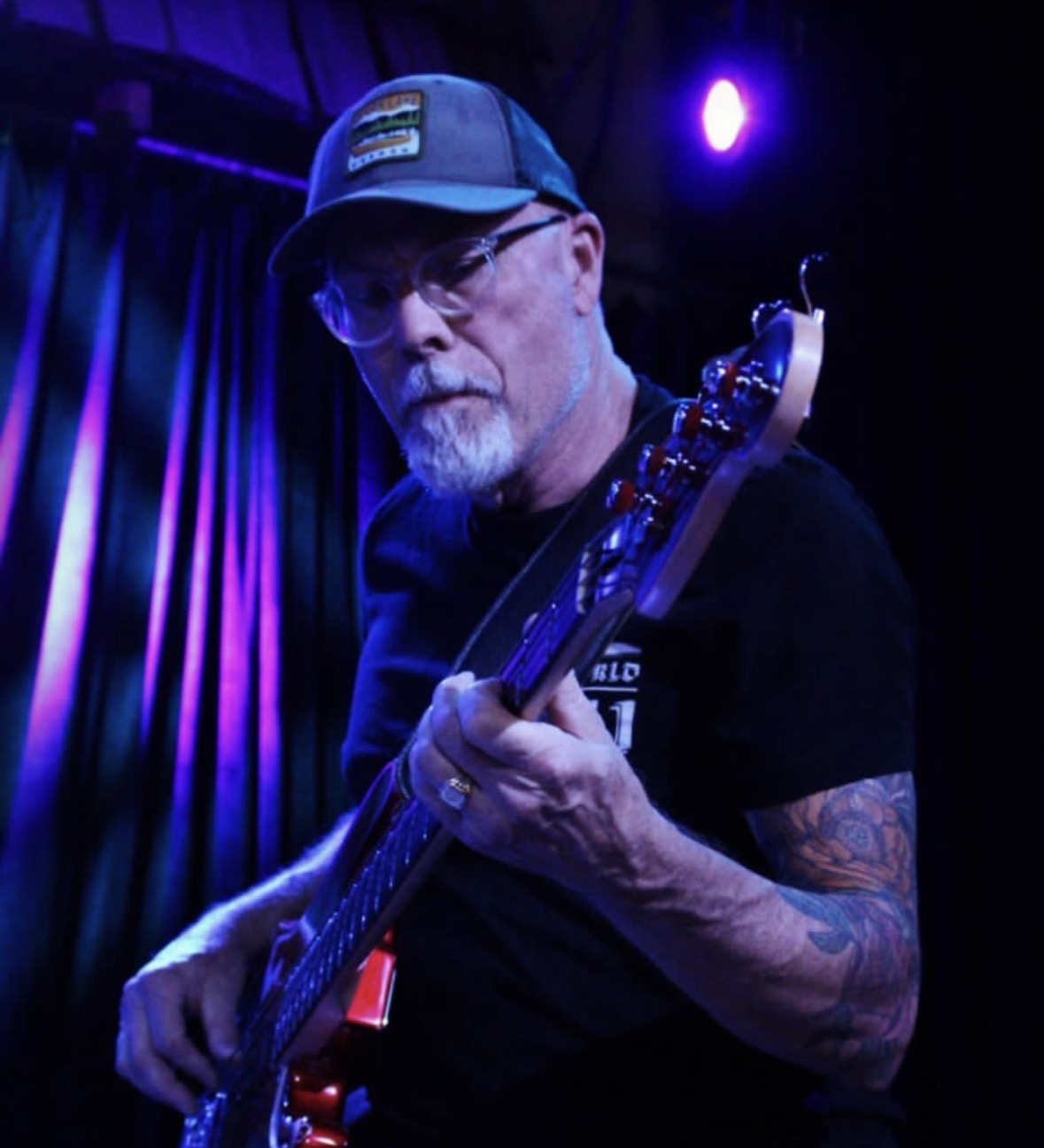 Eric playing a red bass guitar under purple stage lighting